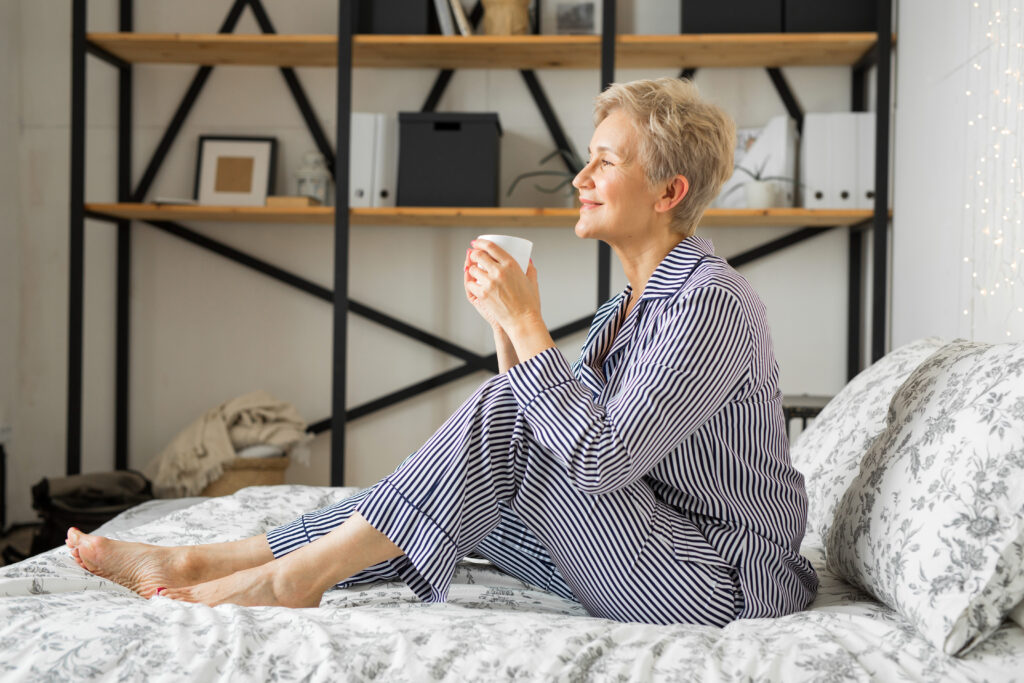 adult elderly woman smiling in pajamas in bed in the bedroom with a mug