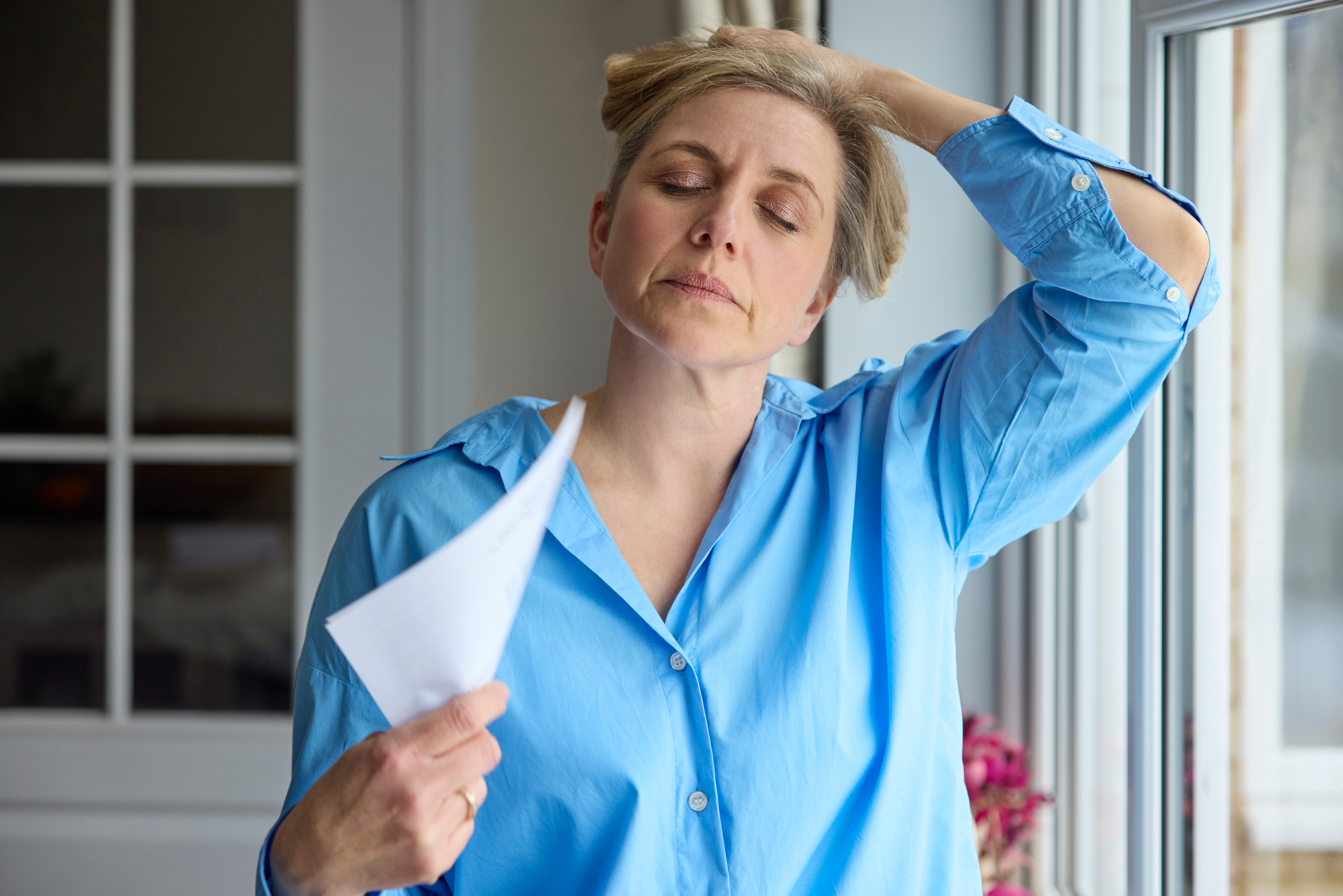 Mature Woman Having Hot Flush At Home Cooling Herself With Letters Or Documents