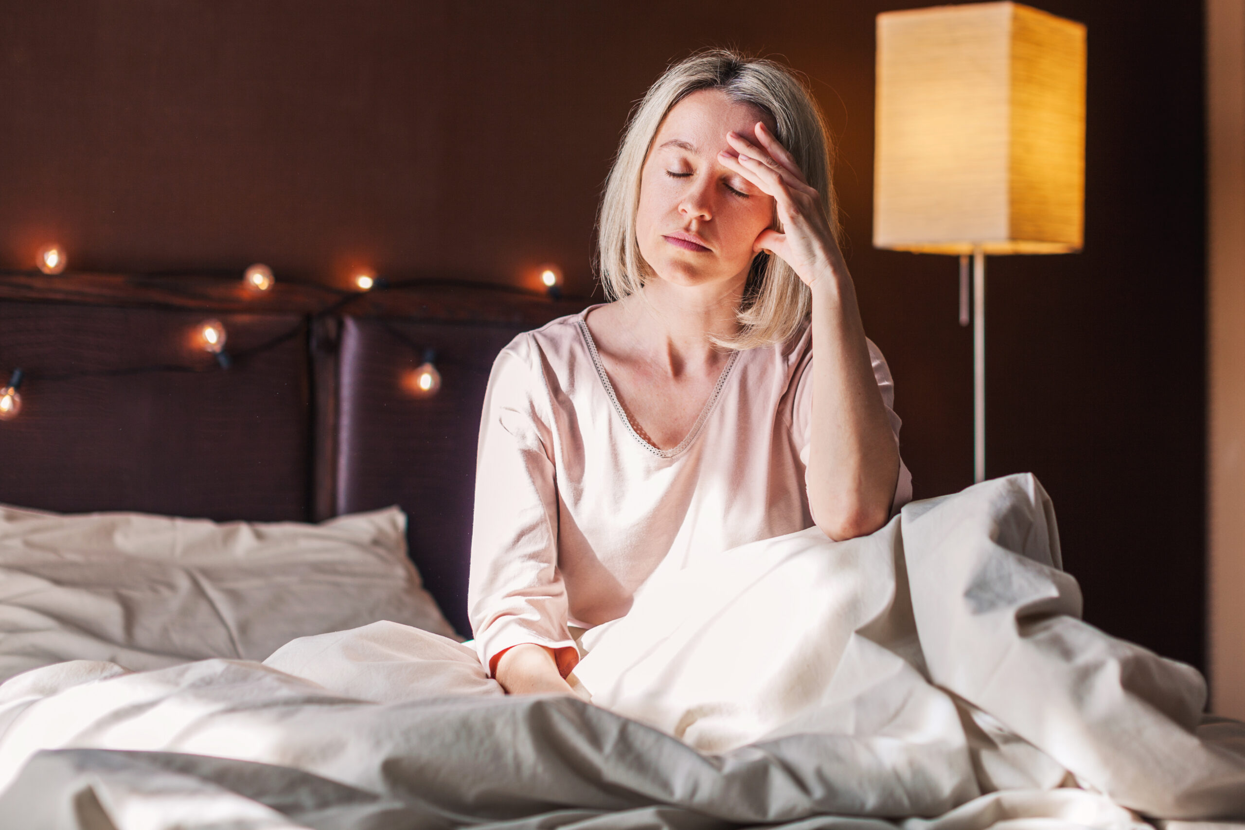 Unhappy sad middle aged woman sitting on bed at home